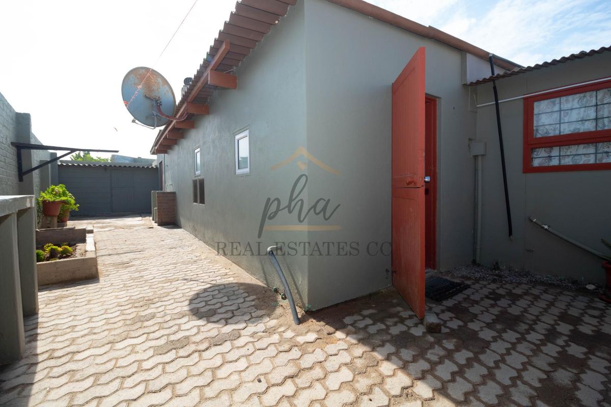 Rear exterior view of the property featuring paved courtyard area, side entrance door, and external wall mounted satellite dish.