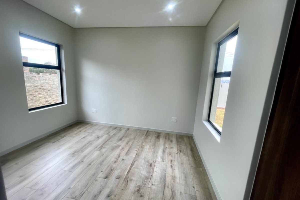 A bright, modern bedroom featuring neutral walls, wood-look laminate flooring, and large windows providing ample natural light.