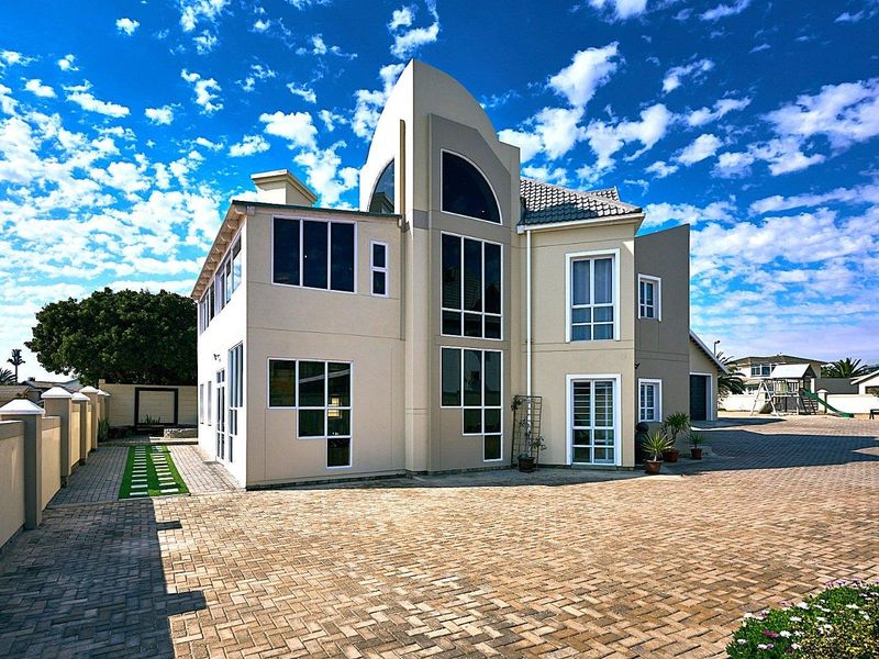 A modern multi-story residential property featuring a large paved driveway, expansive glass windows, and a well-maintained exterior facade.