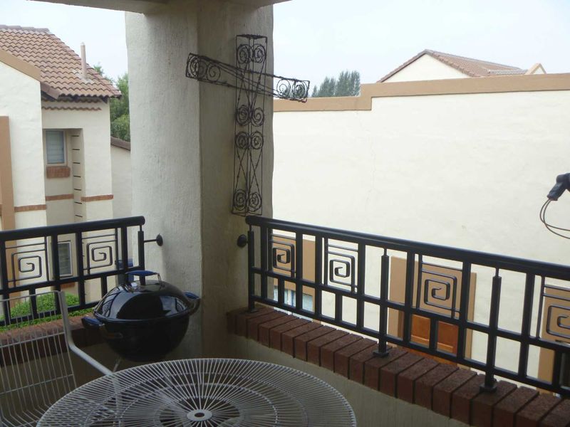 A covered balcony featuring a decorative metal balustrade with a brick base and a concrete support pillar.
