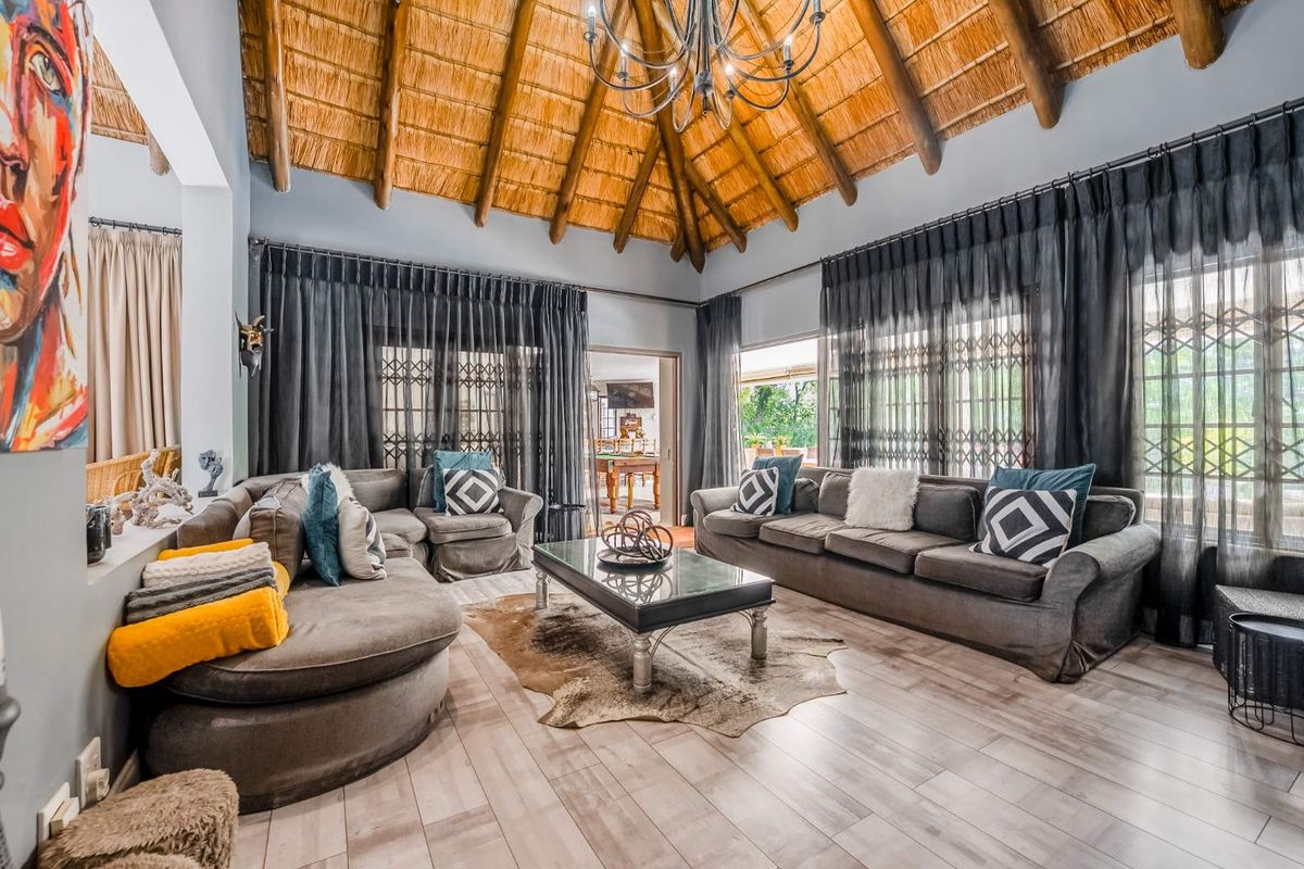 Spacious living room featuring a high vaulted thatched ceiling with exposed timber rafters, laminate flooring, and large sliding doors providing access to the outdoors.