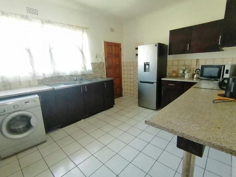 Functional kitchen featuring dark built-in cabinetry, a double sink, tiled backsplash, and a breakfast bar with tiled flooring throughout.