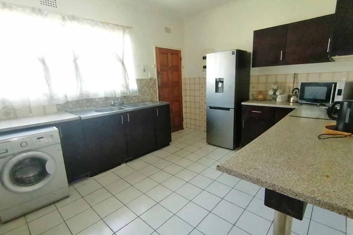 Functional kitchen featuring dark built-in cabinetry, a double sink, tiled backsplash, and a breakfast bar with tiled flooring throughout.