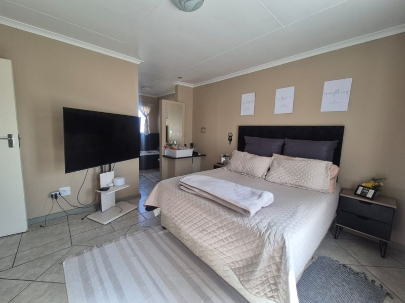 A bedroom featuring tiled flooring, coved ceilings, and an integrated vanity area leading to an en-suite bathroom.