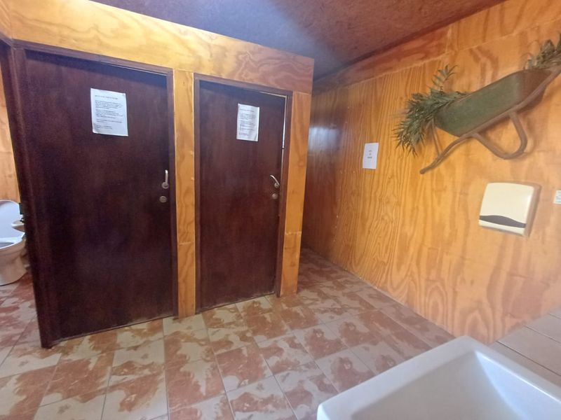 A functional commercial bathroom facility featuring plywood wall paneling, tiled flooring, and two private stalls.