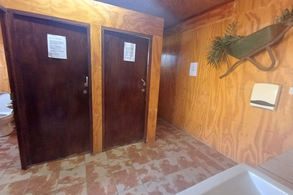 A functional commercial bathroom facility featuring plywood wall paneling, tiled flooring, and two private stalls.