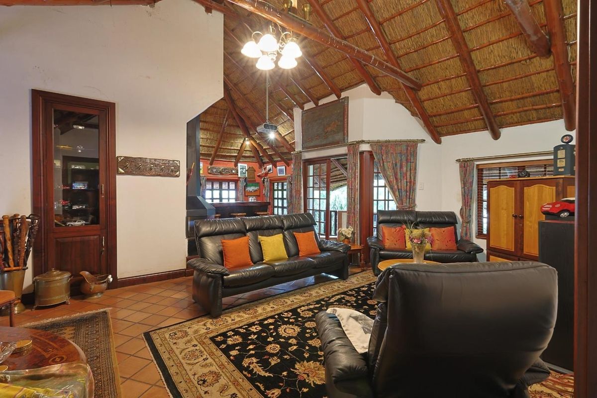 Spacious living room featuring a high vaulted thatched ceiling with exposed timber beams, terracotta floor tiles, and a built-in fireplace.