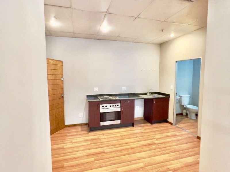 Open plan studio apartment featuring a compact kitchenette with built-in oven and hob, laminate flooring, and an adjacent bathroom.