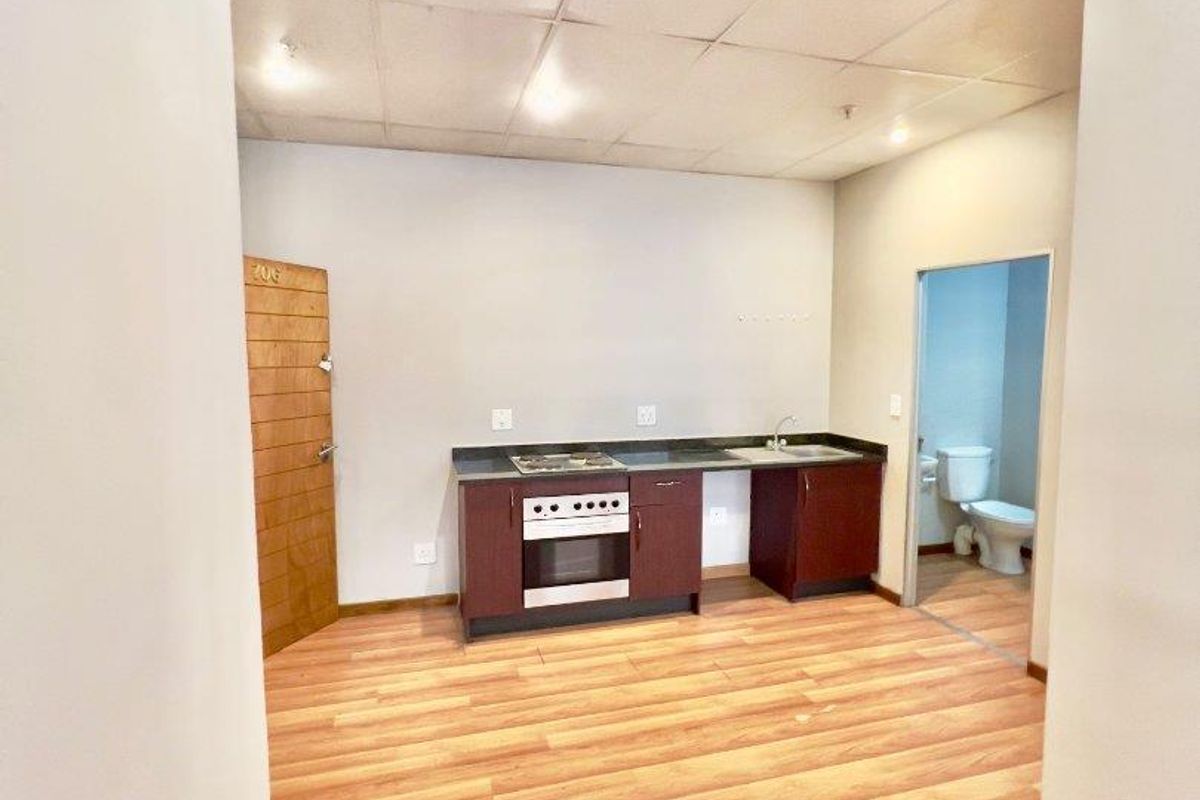 Open plan studio apartment featuring a compact kitchenette with built-in oven and hob, laminate flooring, and an adjacent bathroom.