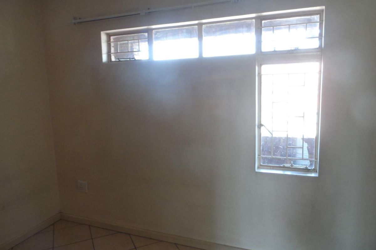 An empty bedroom featuring tiled flooring and windows fitted with security bars, requiring cosmetic updates to the wall finishes.