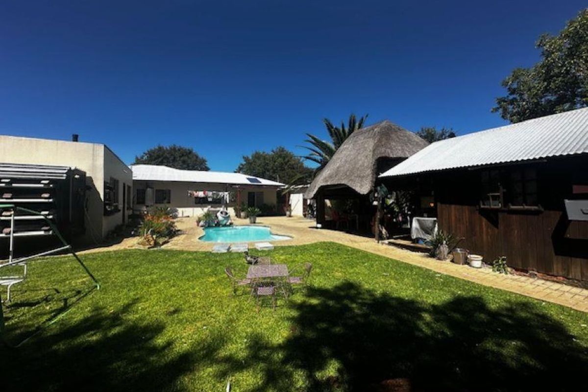 Spacious backyard featuring a swimming pool, a thatched lapa entertainment area, and a well-maintained lawn, offering a private outdoor living space.