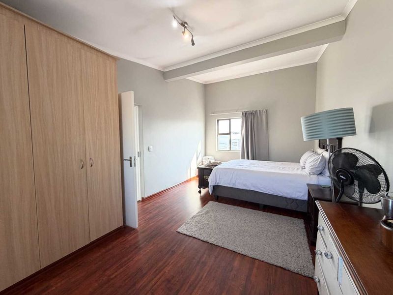 Spacious bedroom featuring warm-toned laminate flooring and ample built-in cupboard storage, offering a comfortable and functional living space.