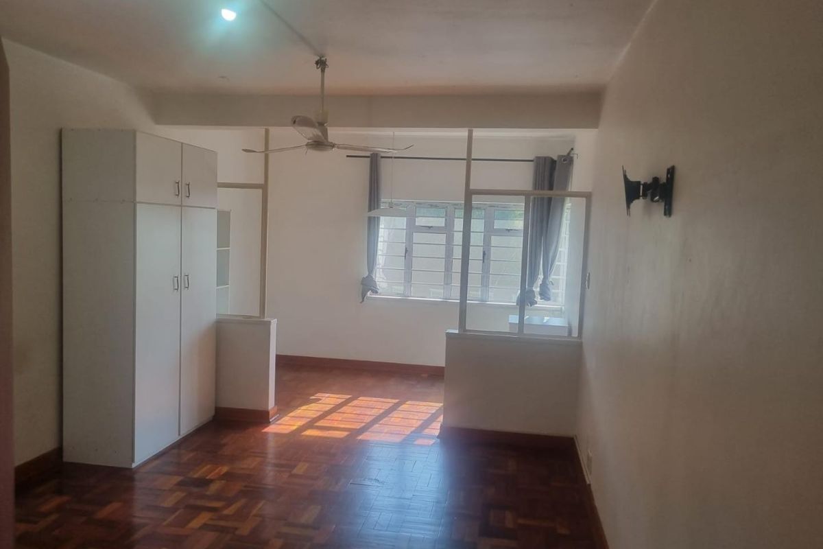 A spacious bedroom featuring original parquet flooring, a built-in wardrobe, and a partition wall, offering a blank canvas for renovation.