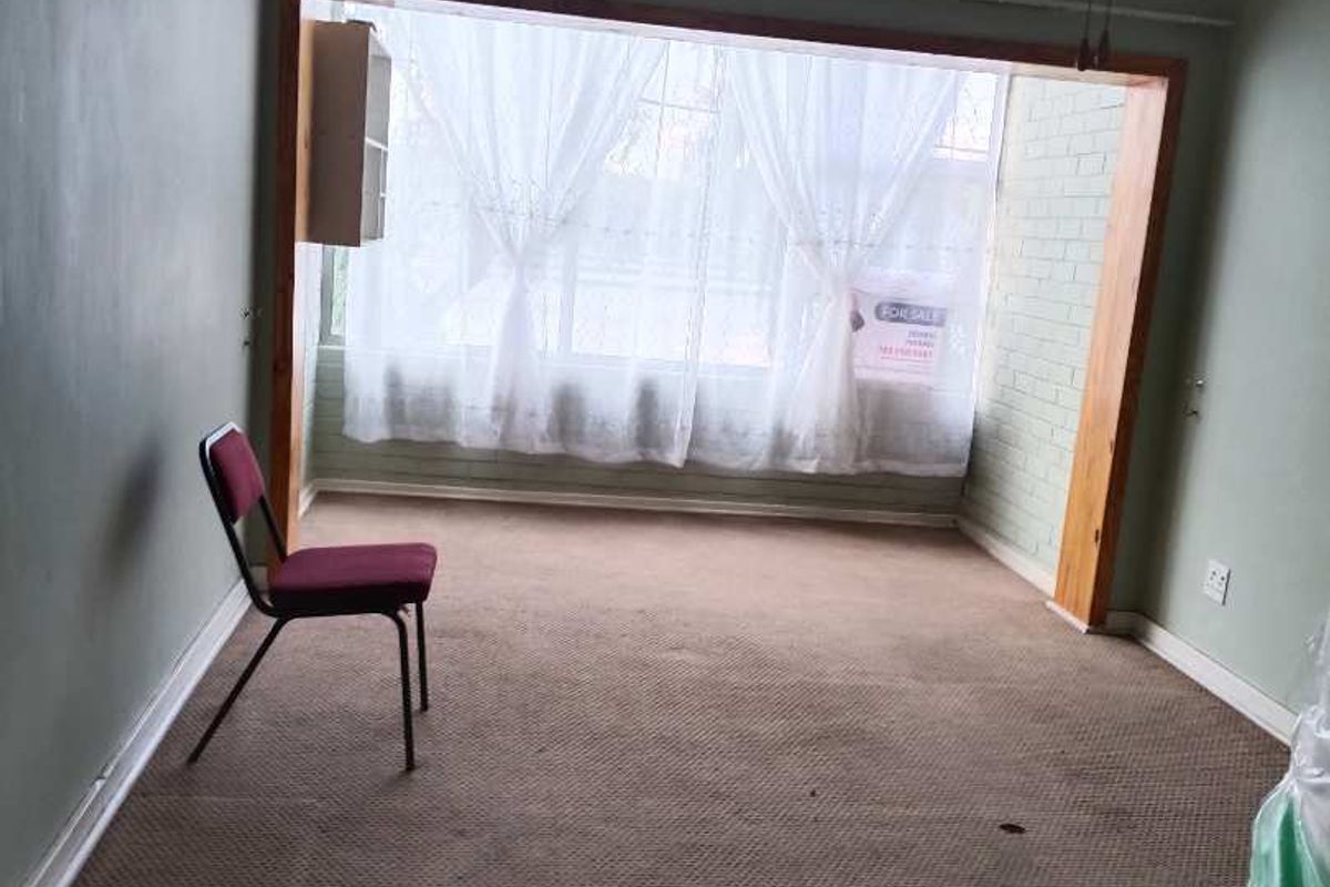 A spacious, empty living room featuring carpet flooring, a large timber-framed window, and a ceiling fan, offering a blank canvas for renovation.