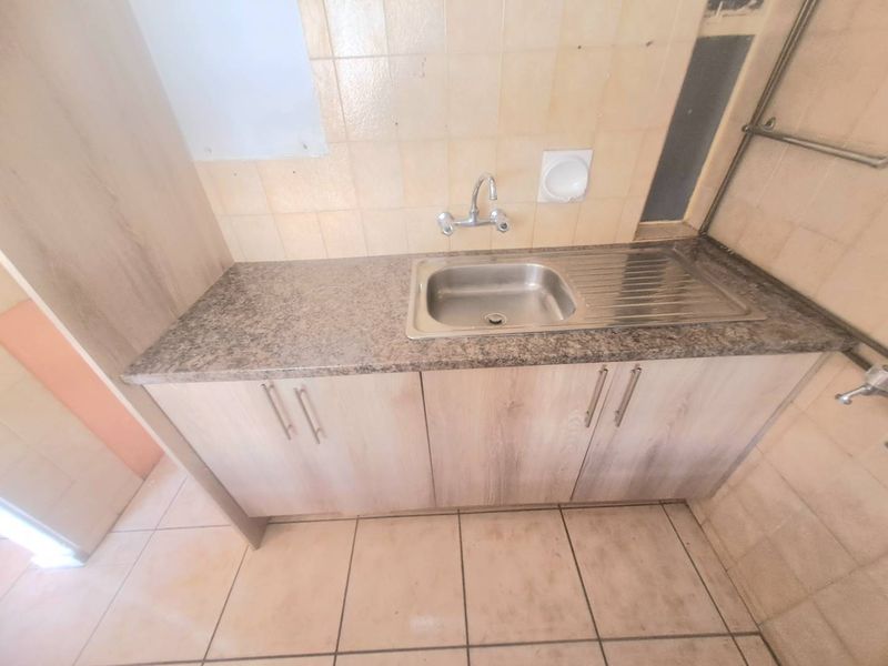 A functional scullery or utility area featuring a stainless steel sink, laminate countertop, base cabinetry, and tiled finishes throughout.