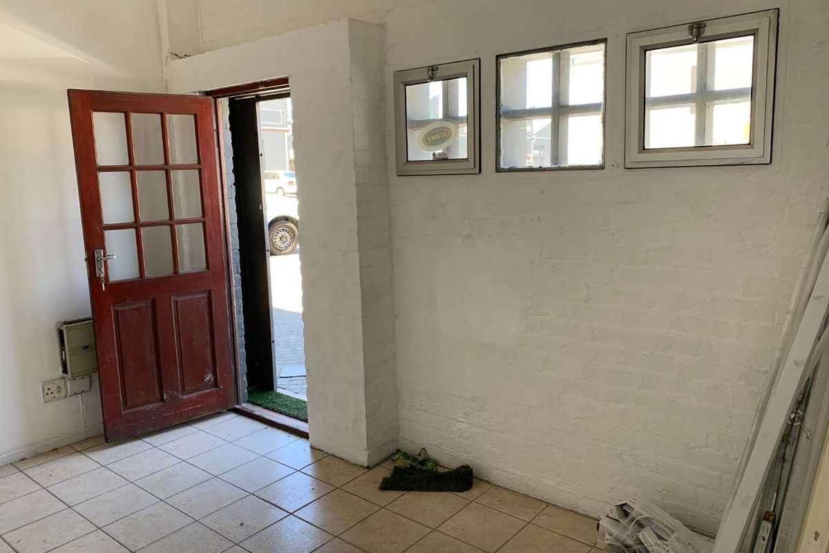 An industrial entry space featuring tiled flooring, a timber-framed glass door, and multiple small square windows set into a painted brick wall.