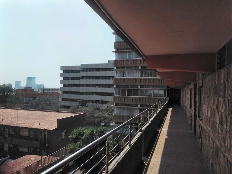 An exterior balcony walkway featuring a metal balustrade and brick walling, overlooking surrounding urban apartment buildings.