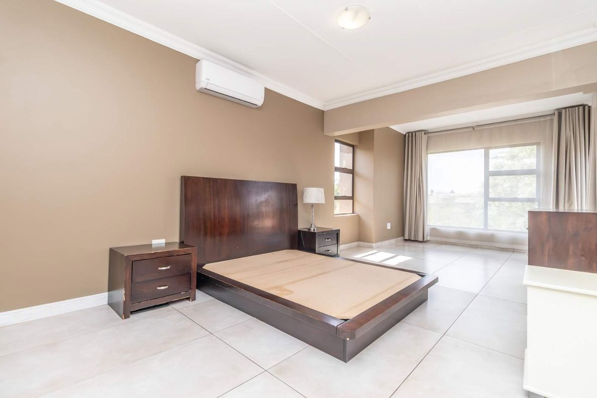 Spacious bedroom featuring neutral wall tones, large windows for natural light, tiled flooring, and a wall-mounted air conditioning unit.
