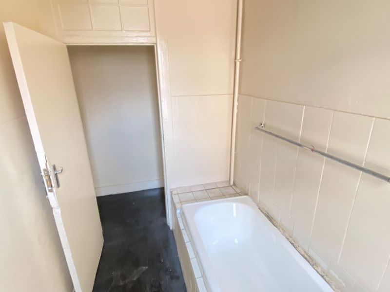 A dated bathroom featuring a built-in bathtub, tiled splashback, and a towel rail, requiring cosmetic updates to modernize the space.