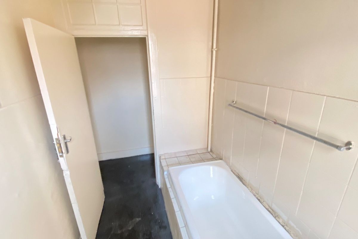A dated bathroom featuring a built-in bathtub, tiled splashback, and a towel rail, requiring cosmetic updates to modernize the space.