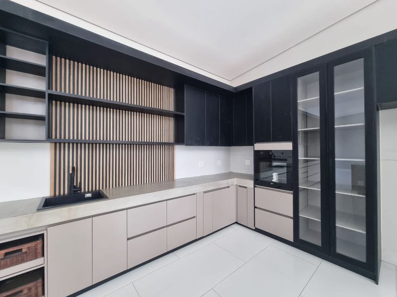 Modern kitchen featuring sleek two-tone cabinetry, integrated oven, stone countertops, and a stylish slatted wood feature wall with open shelving.
