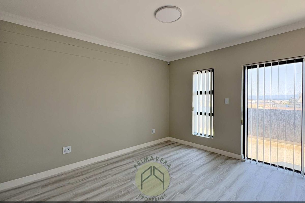 A bright, empty bedroom featuring modern laminate flooring, built-in cupboards, and a sliding glass door providing access to an outdoor balcony area.