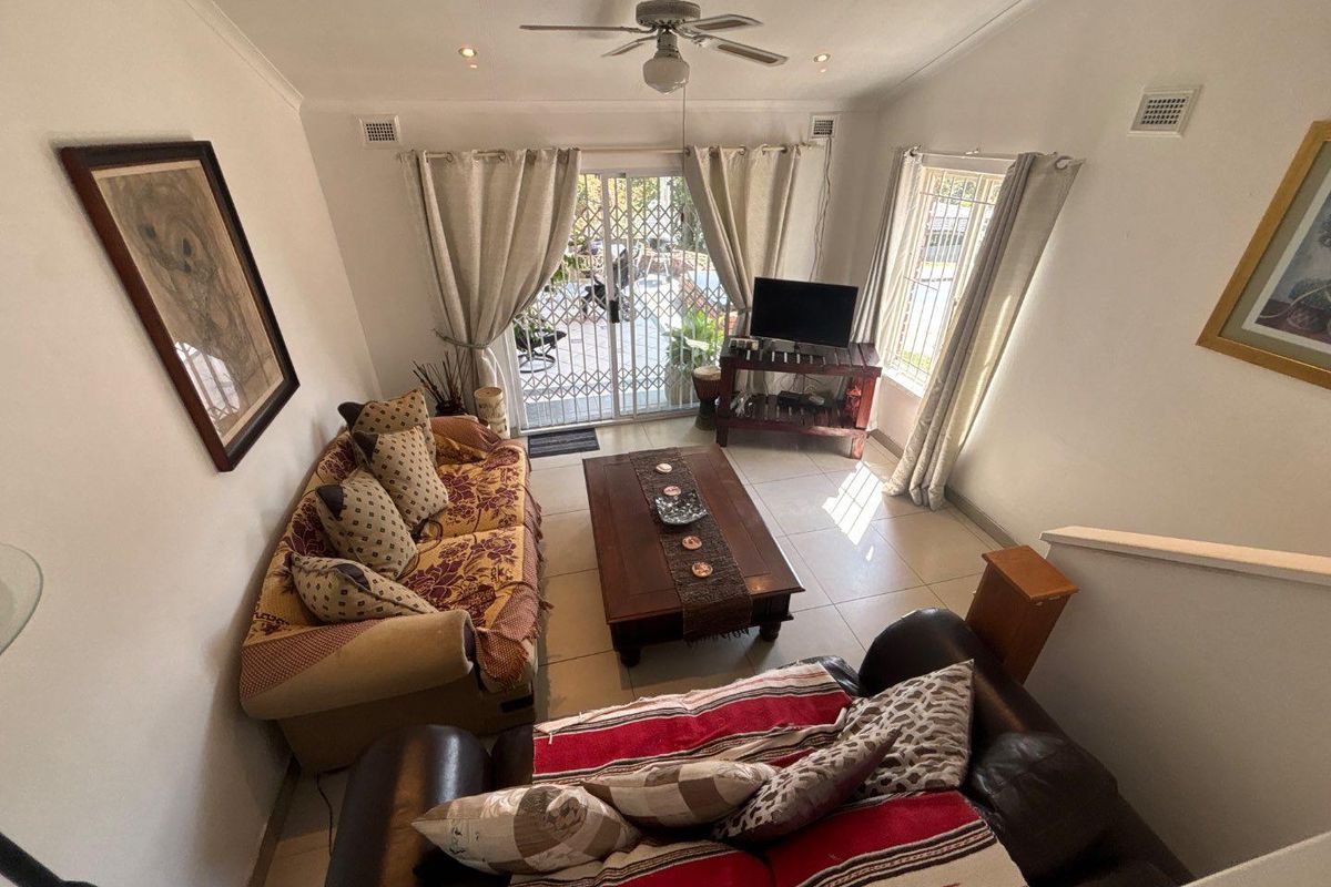 A bright living room featuring tiled flooring, a ceiling fan, and sliding glass doors that provide access to the outdoor area.