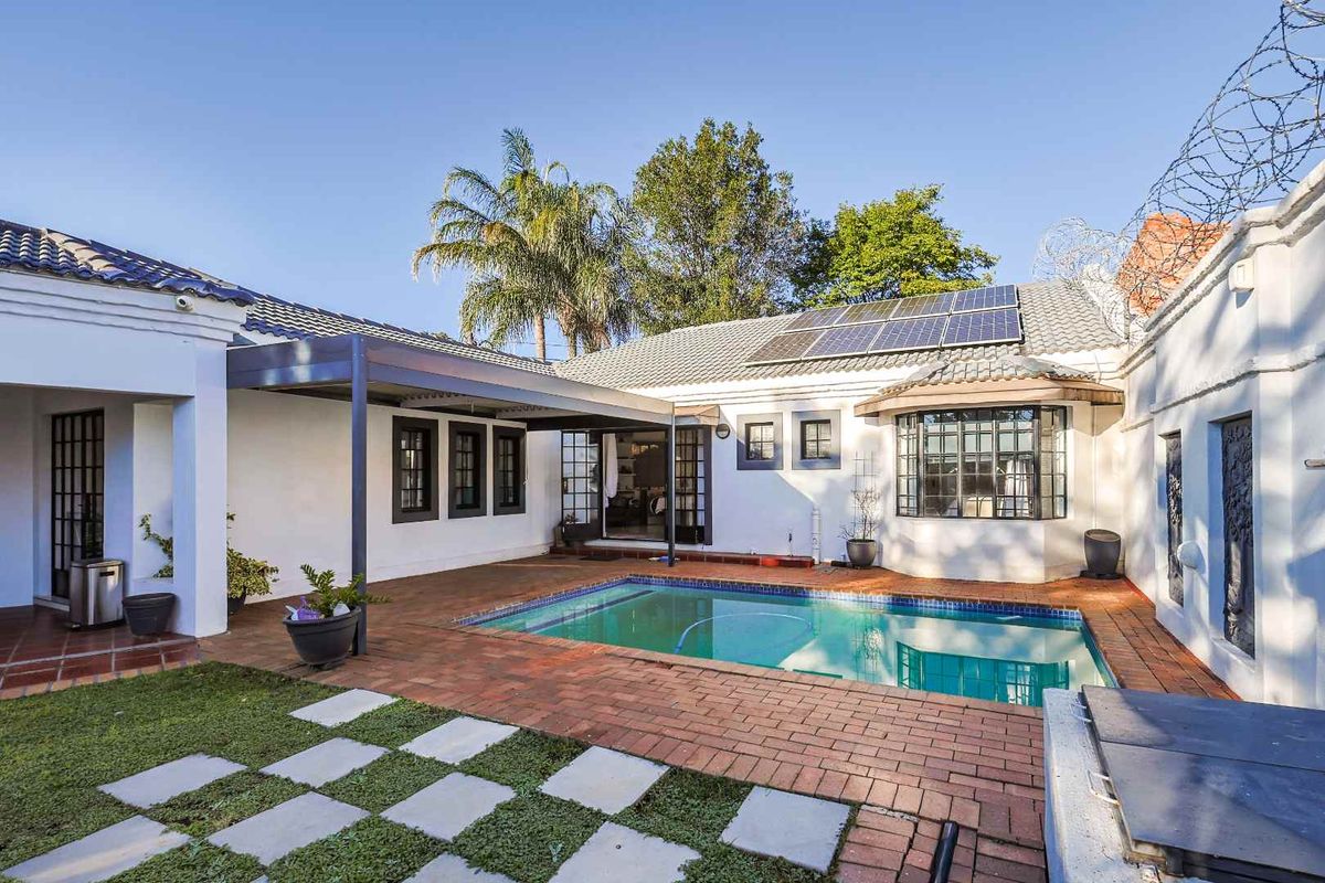 Rear exterior view featuring a swimming pool, paved patio area, covered pergola, and roof-mounted solar panels.