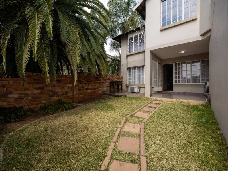 Rear exterior view of the apartment featuring a private garden, paved walkway, covered patio area, and brick boundary wall.