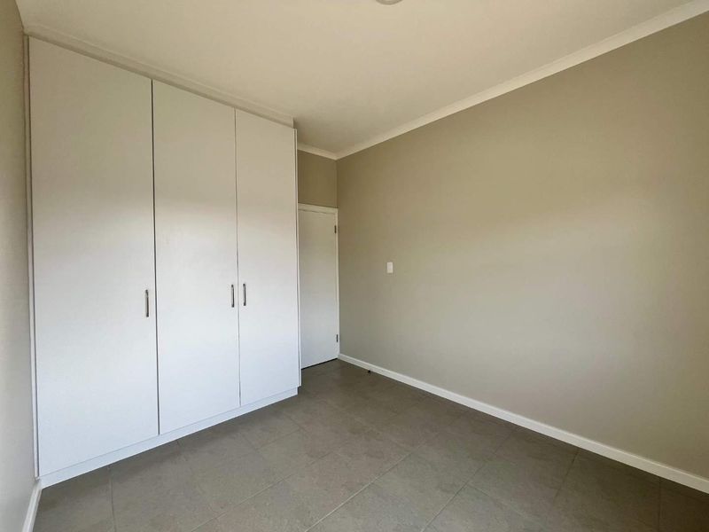A clean, empty bedroom featuring neutral wall tones, tiled flooring, and ample built-in cupboard storage space.