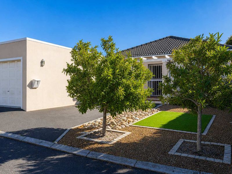 Front view of the property featuring a paved driveway, single garage, and a well-maintained landscaped garden with a security gate entrance.