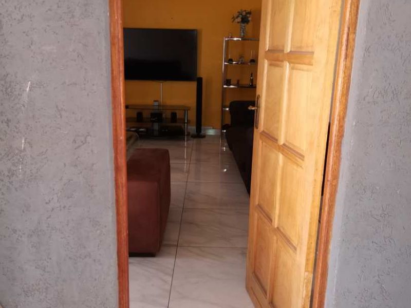 View through a wooden door into a living room featuring tiled flooring and yellow painted walls.