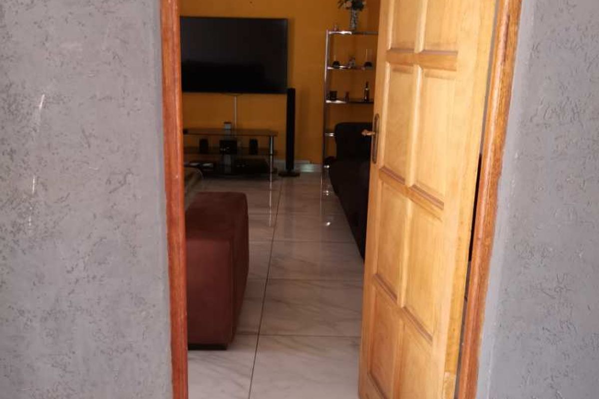View through a wooden door into a living room featuring tiled flooring and yellow painted walls.