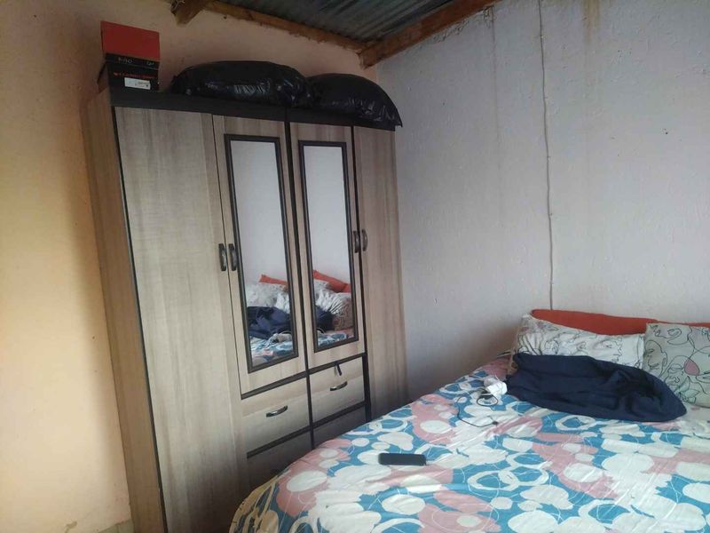A bedroom featuring basic finishes with visible wall staining and an exposed corrugated metal ceiling.