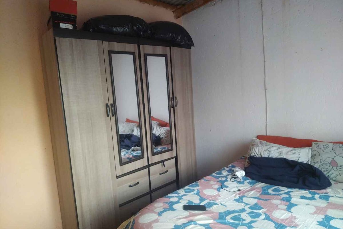 A bedroom featuring basic finishes with visible wall staining and an exposed corrugated metal ceiling.