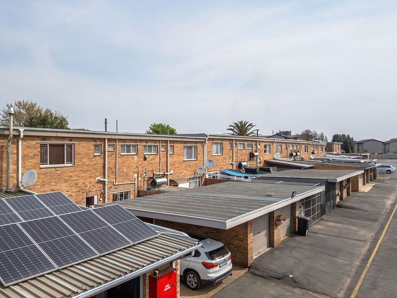 An elevated view of a townhouse complex rear elevation featuring brick facades, multiple garage units, and installed solar panels on the roof.