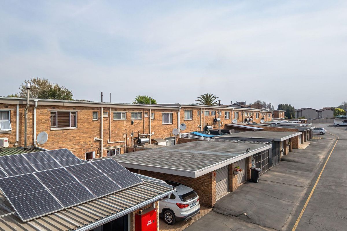 An elevated view of a townhouse complex rear elevation featuring brick facades, multiple garage units, and installed solar panels on the roof.