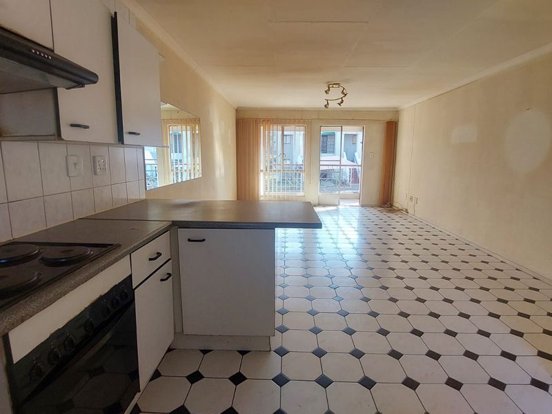 Open-plan kitchen and living area featuring dated cabinetry, electric cooking appliances, and tiled flooring, leading to a sliding door with outdoor access.