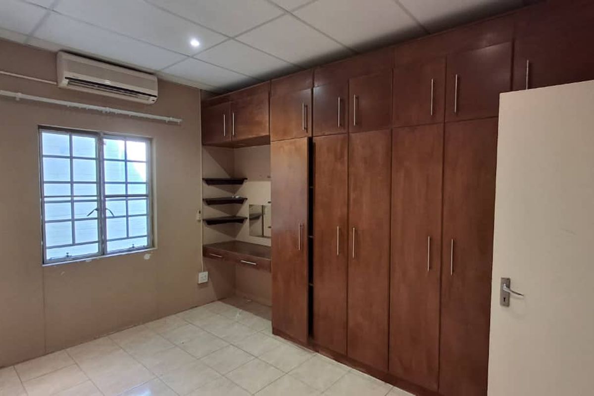 Bedroom featuring extensive built-in wooden cabinetry with integrated desk space, tiled flooring, and a wall-mounted air conditioning unit.