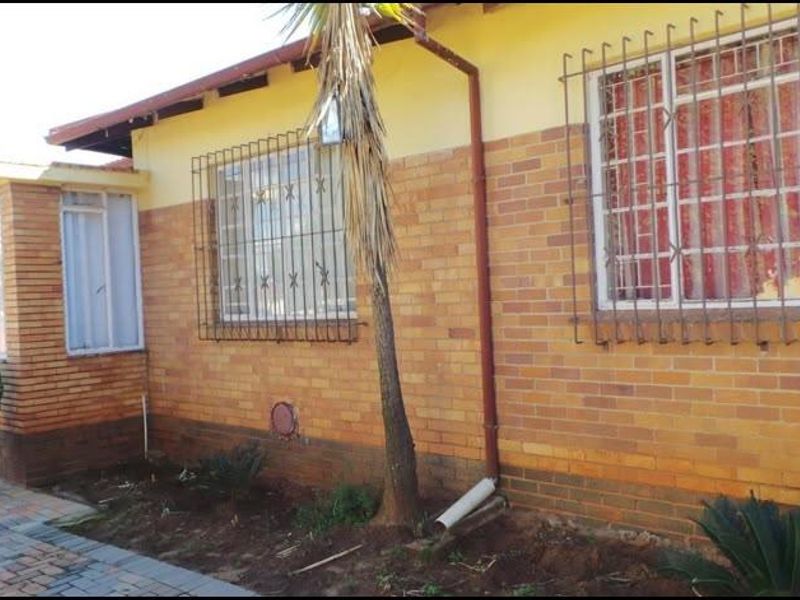 A view of the front exterior featuring face brick walls, security bars on windows, and a paved walkway.