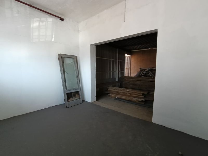 An industrial utility space featuring concrete flooring, exposed fire sprinkler piping, and an open transition to a secondary storage area with metal wall cladding.
