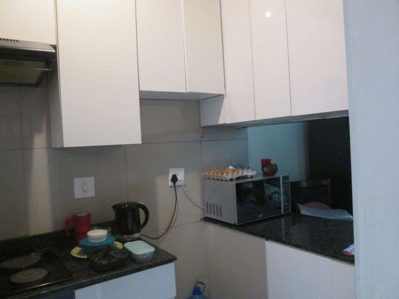 Compact kitchen featuring white cabinetry, granite countertops, and a tiled backsplash, equipped with a built-in hob and extractor fan.