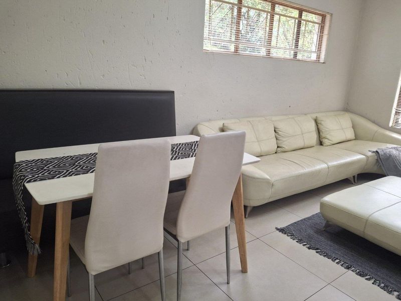 A living area featuring neutral tiled flooring and horizontal window blinds, providing a functional and well-lit space.