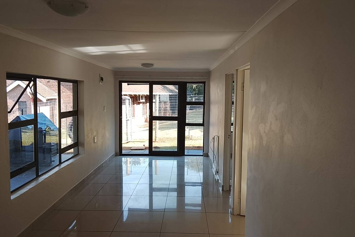 An empty, open-plan living area featuring polished floor tiles, large aluminium-framed windows, and a sliding glass door leading to the exterior.