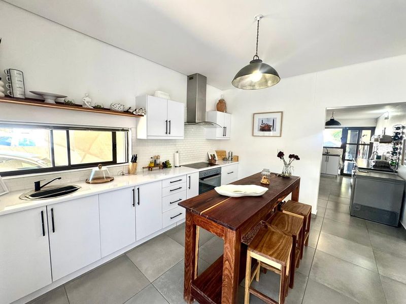Modern kitchen featuring white cabinetry, subway tile backsplash, stainless steel appliances, stone countertops, and a central wooden island with pendant lighting.