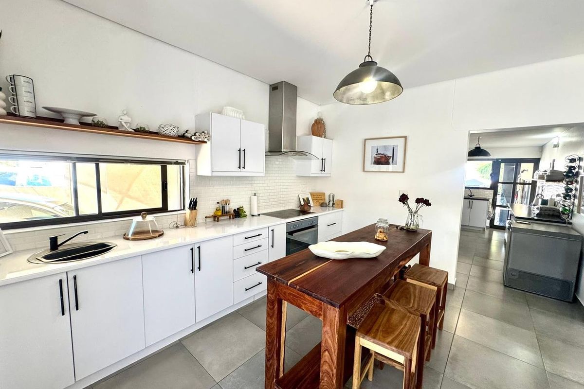 Modern kitchen featuring white cabinetry, subway tile backsplash, stainless steel appliances, stone countertops, and a central wooden island with pendant lighting.