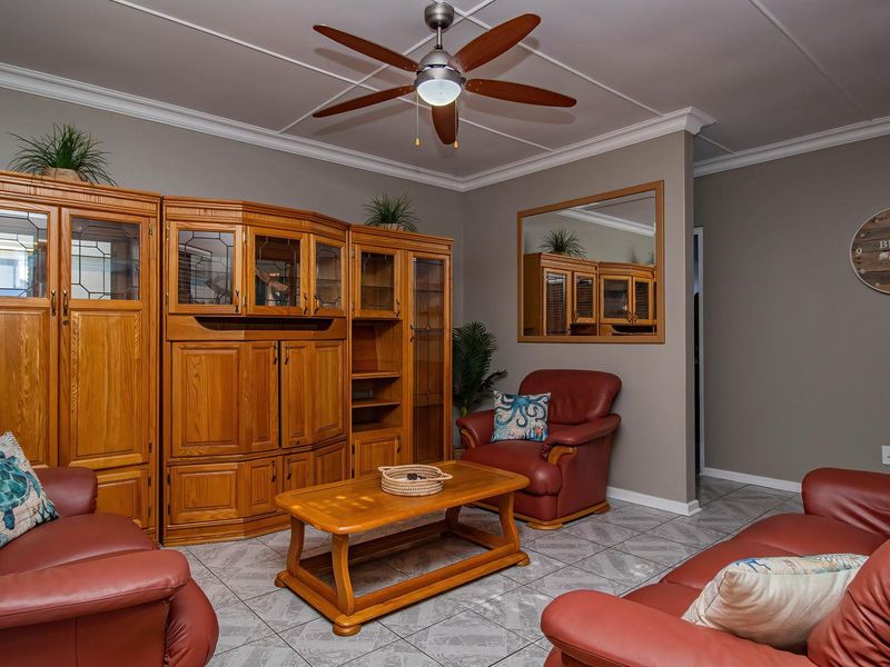 A living room featuring tiled flooring, crown molding, and a ceiling fan, providing a functional space for relaxation.