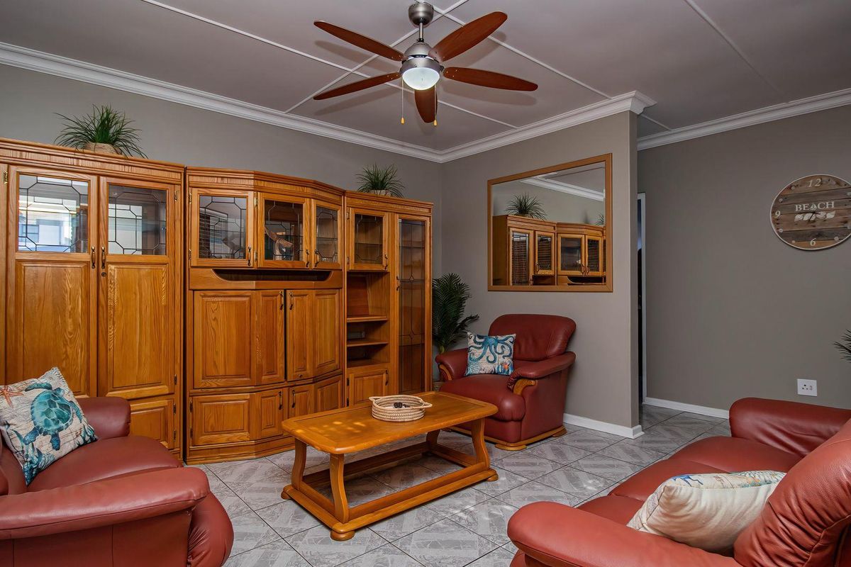 A living room featuring tiled flooring, crown molding, and a ceiling fan, providing a functional space for relaxation.