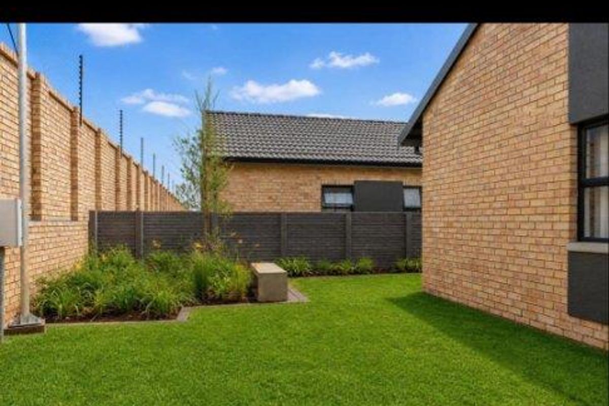 A well-maintained rear garden featuring a manicured lawn, brick boundary walls with electric fencing, and neat landscaping.