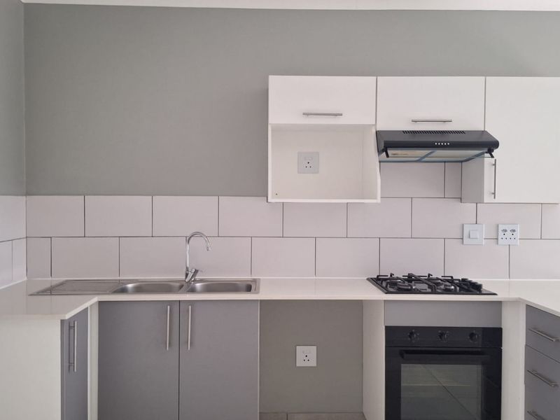 Modern kitchen featuring grey and white cabinetry, stone countertops, a gas hob, built-in oven, extractor fan, and a stainless steel sink with tiled splashback.
